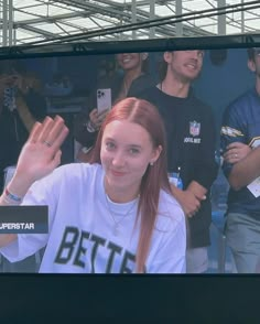 a woman with red hair is smiling and waving at the camera while people are standing behind her