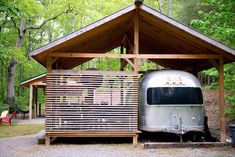 an airstream sits in the woods next to a picnic table with chairs around it