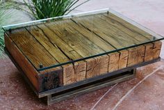 a wooden table with glass top sitting on the ground next to a potted plant