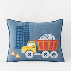 a blue pillow with a dump truck and construction cones on the side, along with a cityscape in the background