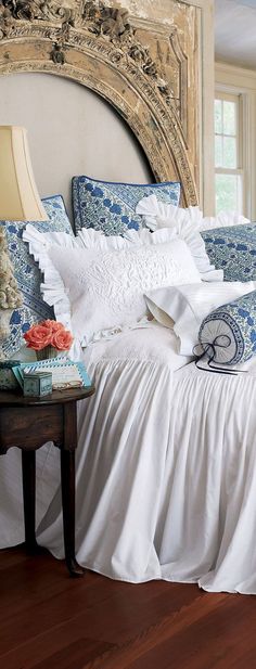 a white bed with blue and white pillows on top of it next to a mirror