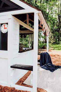 a white outhouse with a clock on the wall and black bench in front of it