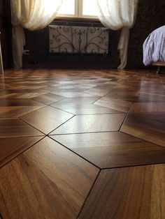 a wooden floor in front of a window with curtains on the windowsill and a bed next to it