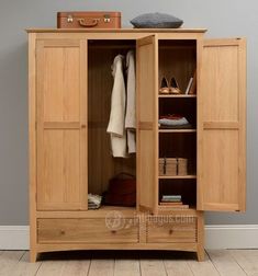 an open wooden cabinet with clothes and shoes in it on the floor next to a wall