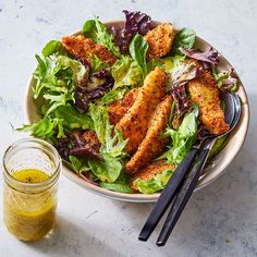 a salad with chicken on it and two chopsticks in front of it next to a jar of mustard