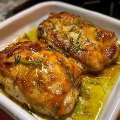 two pieces of chicken sitting on top of a white plate covered in sauce and herbs