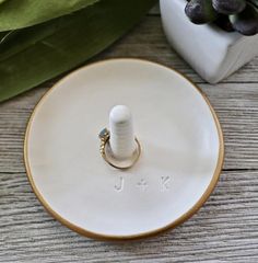 a white ring dish with the word j k on it and a green plant in the background