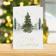 a merry christmas card on a table with a tree and lights in the back ground