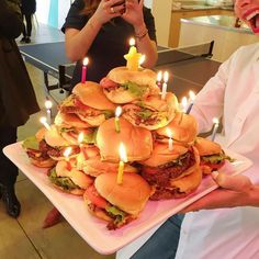 a man holding a plate with many hamburgers on it and lit candles in the middle