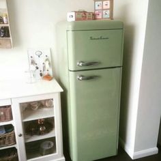 a green refrigerator sitting in the corner of a room next to a white cabinet and shelf