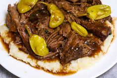 a white plate topped with mashed potatoes covered in beef and peppers on top of gravy