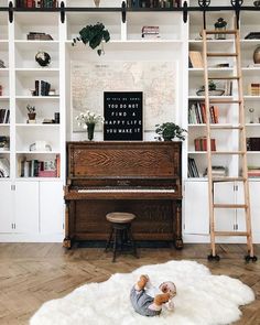 a baby playing on the floor in front of a piano and bookshelf with shelves