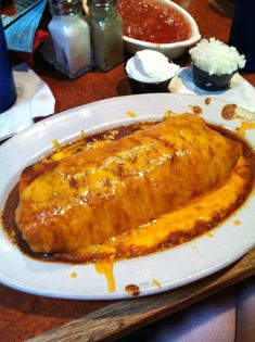 an enchilada covered in cheese on a white plate with sauce and other condiments