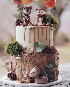 a cake decorated with animals and balloons on top of a wooden table next to a tree stump