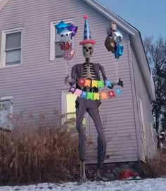 a skeleton is standing in front of a house with balloons attached to his head and wearing a party hat