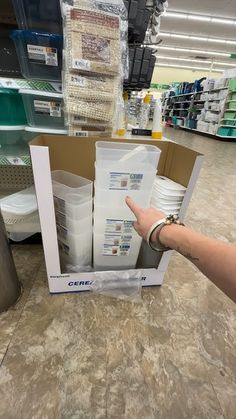 a person is pointing at some cups in a cardboard box on the floor inside a store