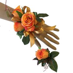 two orange roses and green leaves are attached to a pair of gloves with gold ribbons