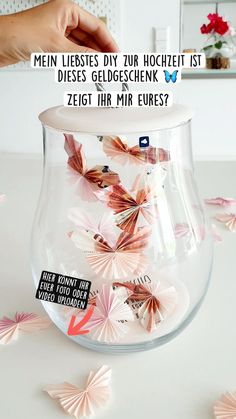 a vase filled with lots of pink flowers on top of a white table next to a person's hand