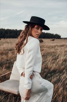 a woman in a white suit and black hat is posing for a photo on a field