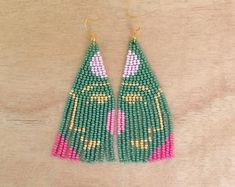 green and pink beaded earrings with gold accents on a wooden table next to a pair of scissors