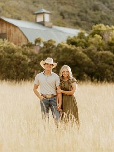 a man and woman standing in tall grass with a barn in the back ground behind them