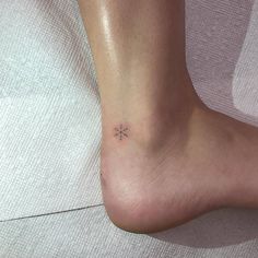 a small snowflake tattoo on the foot of a woman's left ankle