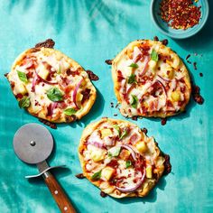 three small pizzas sitting on top of a blue table next to a spatula