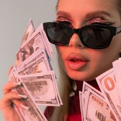 a woman wearing sunglasses holding up money in front of her face and looking at the camera