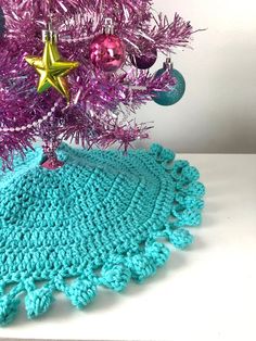 a crocheted doily next to a pink christmas tree with purple and blue ornaments