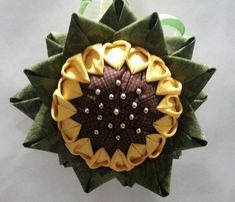 a green and yellow brooch sitting on top of a white table next to a ribbon