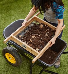 a woman pushing a wheelbarrow full of dirt and plants in it's tray