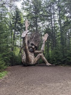 a large wooden sculpture sitting on top of a dirt road in the middle of a forest