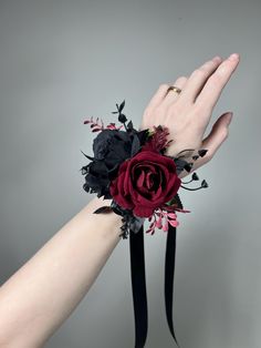 a woman's hand is holding a red and black wrist corsage