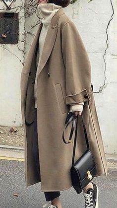 a woman walking down the street with a handbag in her mouth and wearing a coat