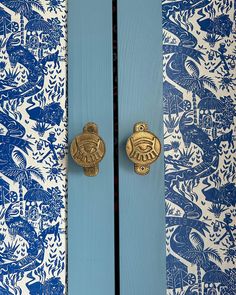 two blue and white doors with gold handles in front of a wallpapered background