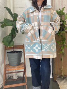 a woman standing in front of a potted plant wearing a blue and white coat