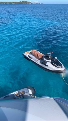 a man is laying on the back of a boat in clear blue water with an island in the background