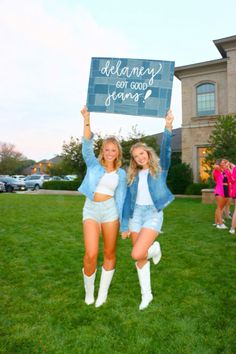 two young women holding up a sign in the grass