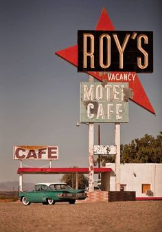 an old car is parked in front of a motel and cafe sign with a red star on top