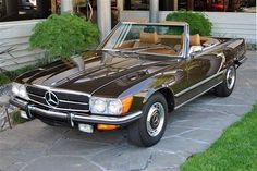 a brown mercedes benz is parked in front of a building with green grass and bushes