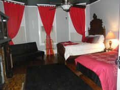 a bed room with a neatly made bed and red drapes hanging from the ceiling