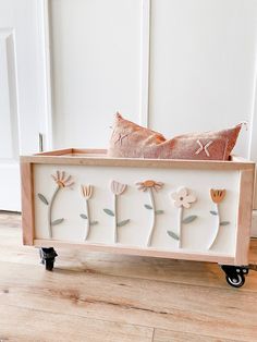 a wooden box with flowers on it and a pillow in the middle, sitting on top of a hard wood floor