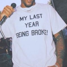 a man holding a microphone and wearing a t - shirt that says my last year being broke