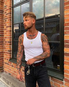 a man with tattoos standing in front of a brick building