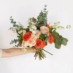 a person's hand holding a bouquet of flowers on a white background with greenery