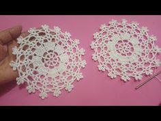 two white doilys are being made with crocheted thread and yarn on a pink surface