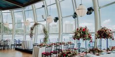 the tables are set up for an event with flowers and greenery on them, along with lanterns hanging from the ceiling