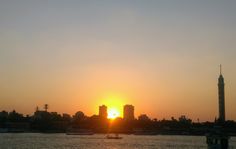 the sun is setting over some buildings and boats on the water in front of it