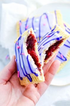 a hand holding a pastry with purple icing and sprinkles