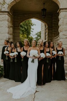 a group of women standing next to each other in front of a stone archway with flowers